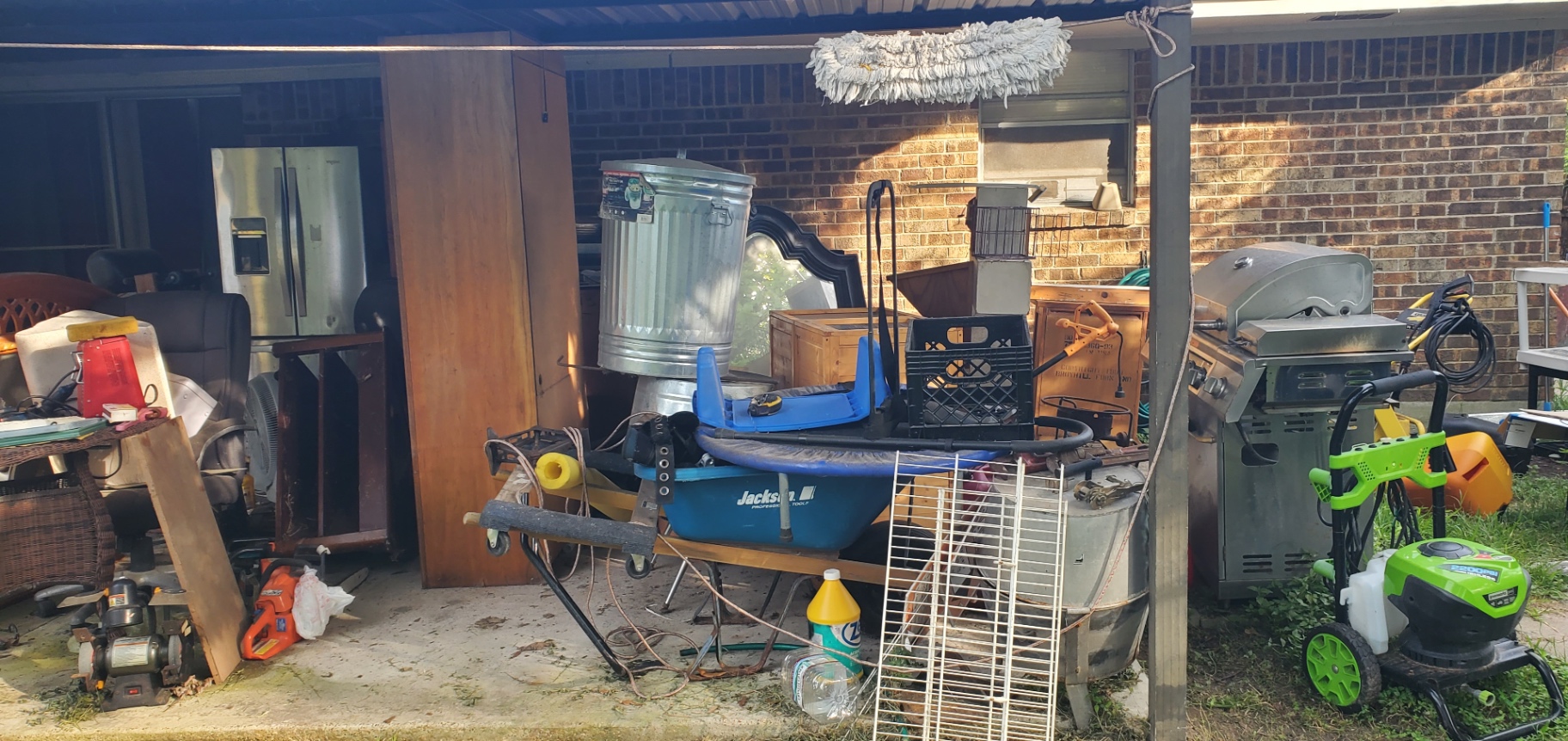 Before — cluttered Houston carport with trampoline, trash can, grill, and mixed household junk before Holman Hauling cleanout